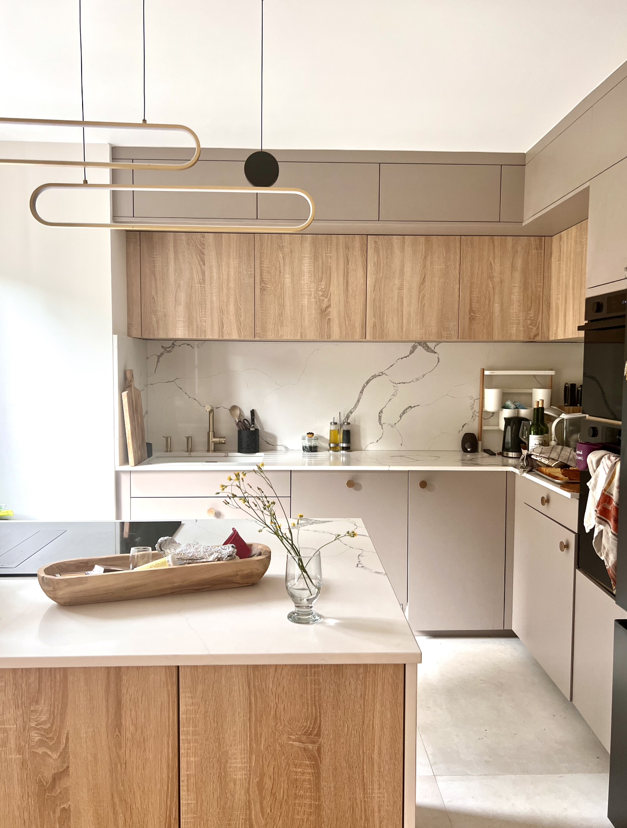 Modern kitchen with light wood and white cabinetry, marble backsplash, and minimalist decor.