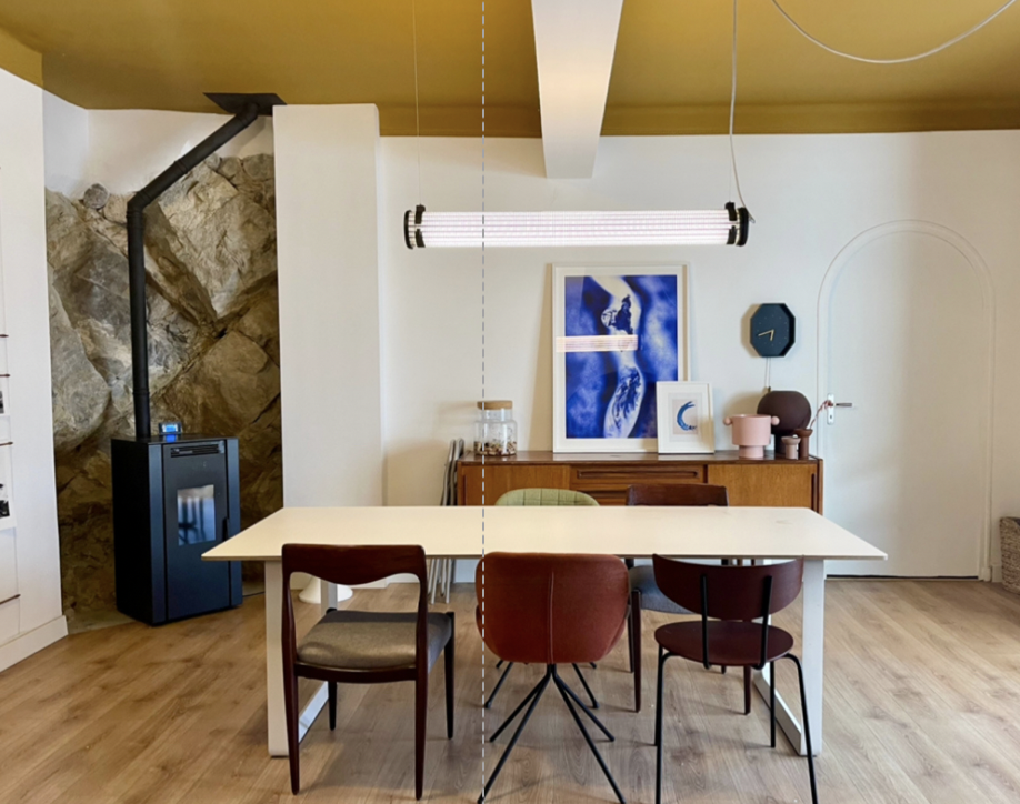 Interior of a dining room with a white table, four chairs, a wood sideboard with framed artwork, and a black wood stove against a stone wall on the left.