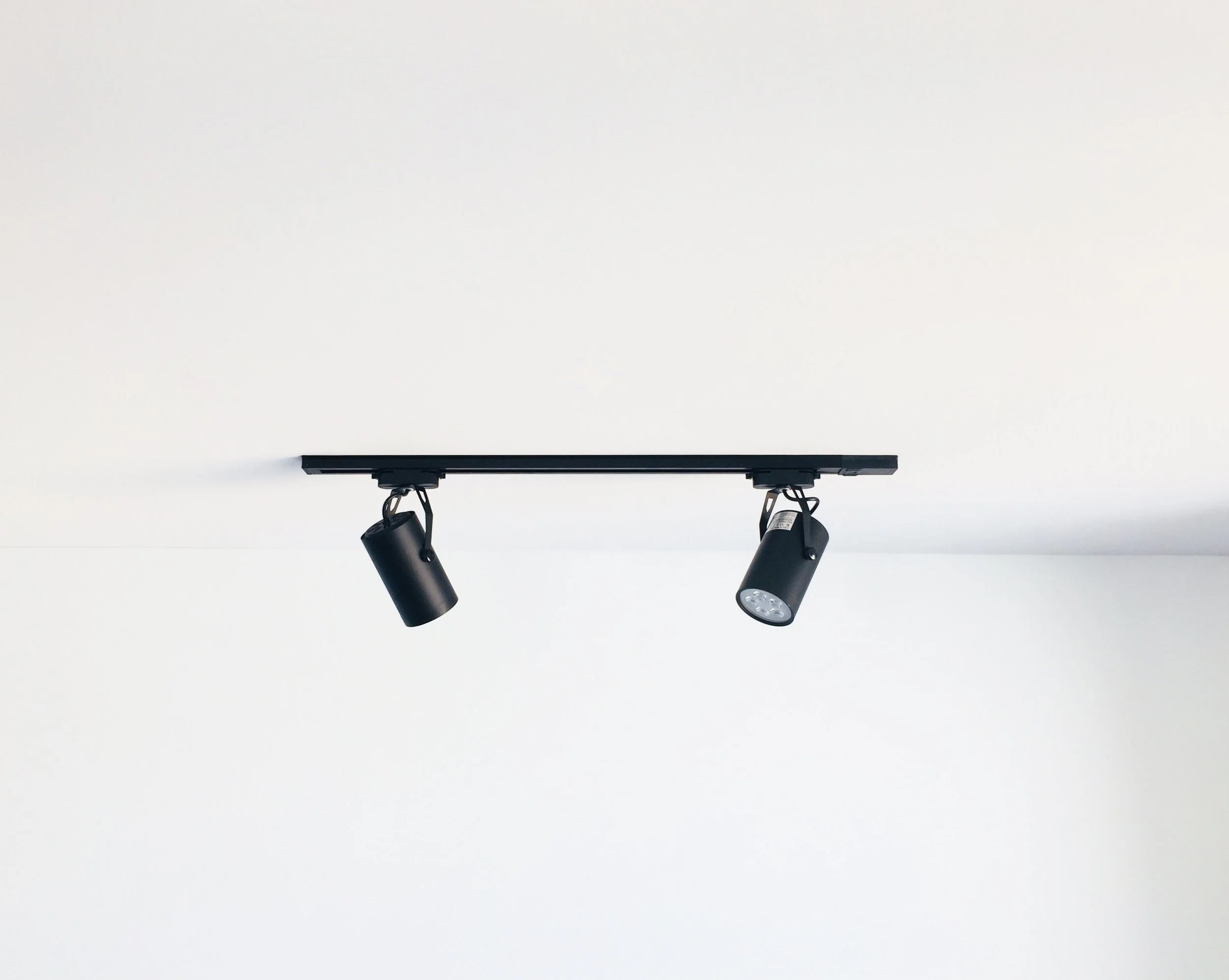 Ceiling-mounted black track lighting with two adjustable spotlights on a white ceiling.