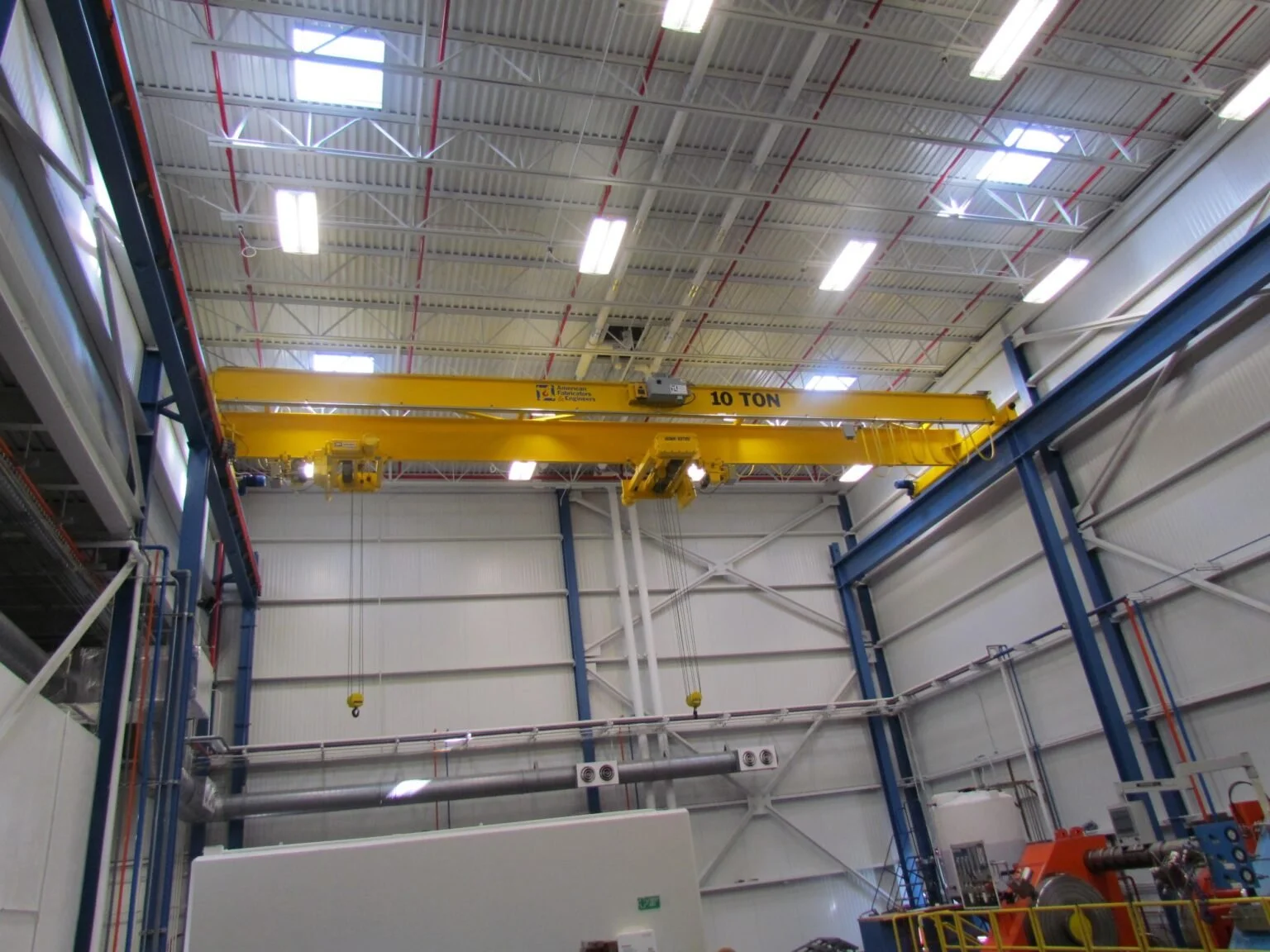 Green overhead crane rated for 10 tons inside an industrial facility, with structural steel walls, pipes, and machinery.