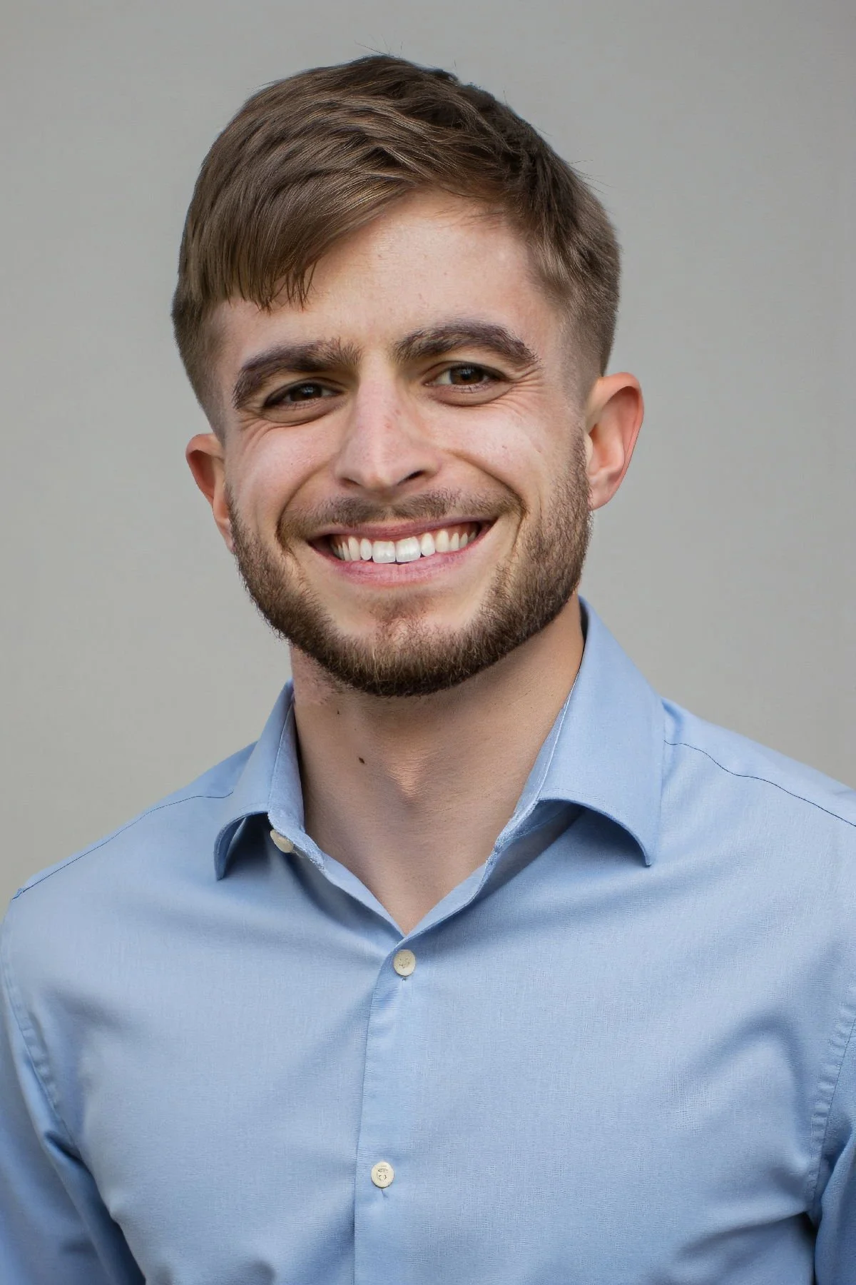 Profile picture of Jacob Ortlieb, a young man with brown hair, beard, and mustache, smiling, wearing a light blue collared shirt, against a plain gray background.