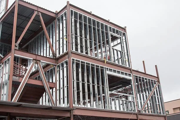 Under construction building with metal framing and wooden stairs, multiple floors, overcast sky.