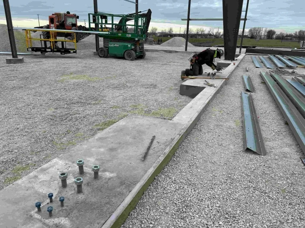 Construction worker installing a concrete foundation with metal beams and bolts at a building site.