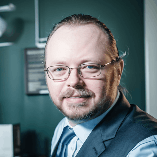 Profile picture of Timothy Looper with long hair, glasses, and a goatee wearing a suit jacket and light blue shirt, sitting in an office with computer screens in the background.