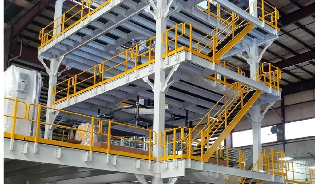 Multi-level industrial structure with yellow safety railings and stairs inside a warehouse or factory.