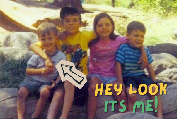 Four children sitting on a rock outdoors, smiling. One boy in a yellow shirt has his arm around a girl in a pink shirt, and another boy in a blue striped shirt is on the end. Text overlay says "Hey Look It's Me!" in colorful letters.