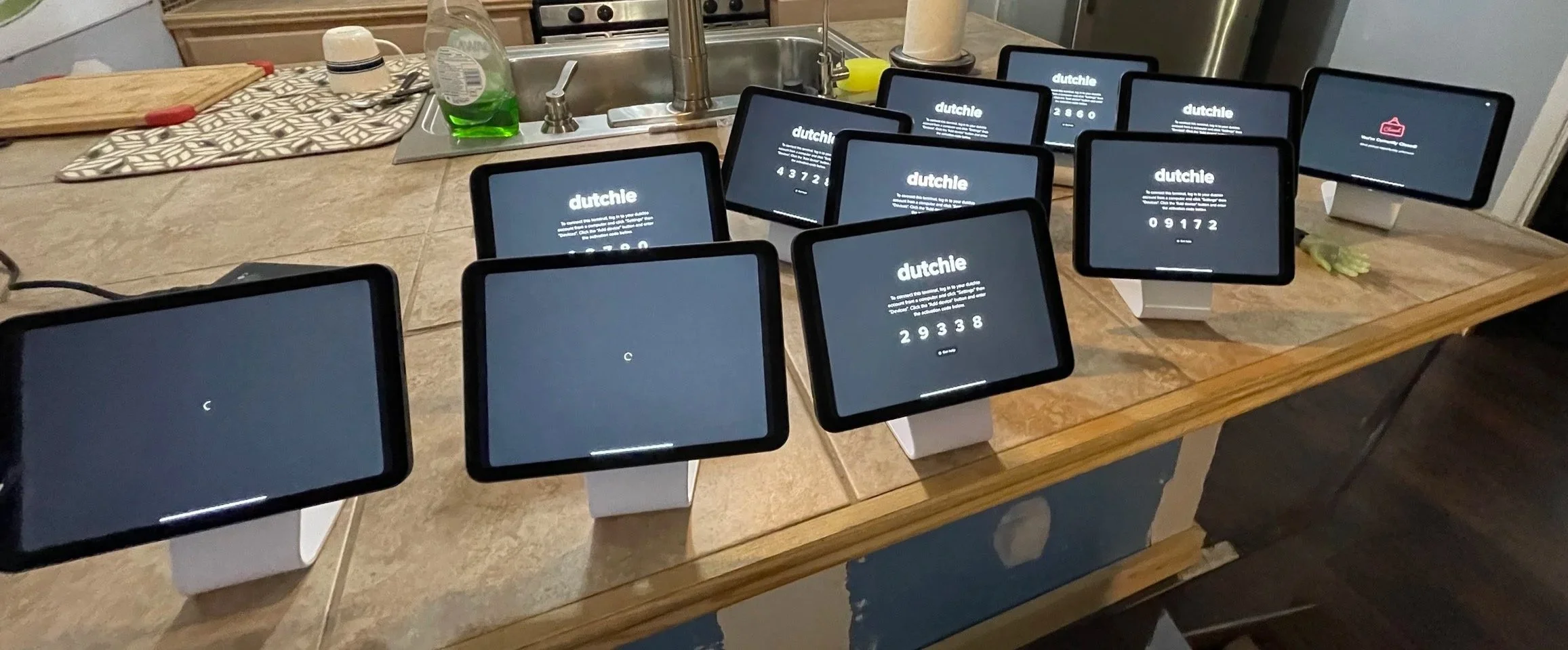 Several touchscreen kiosks on a kitchen counter displaying the Dutchie cannabis dispensary login screen, with some screens showing error messages and others showing serial numbers.