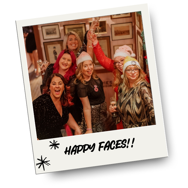 Group of women celebrating, some wearing Santa hats, holding drinks, smiling, and having fun at a festive gathering.