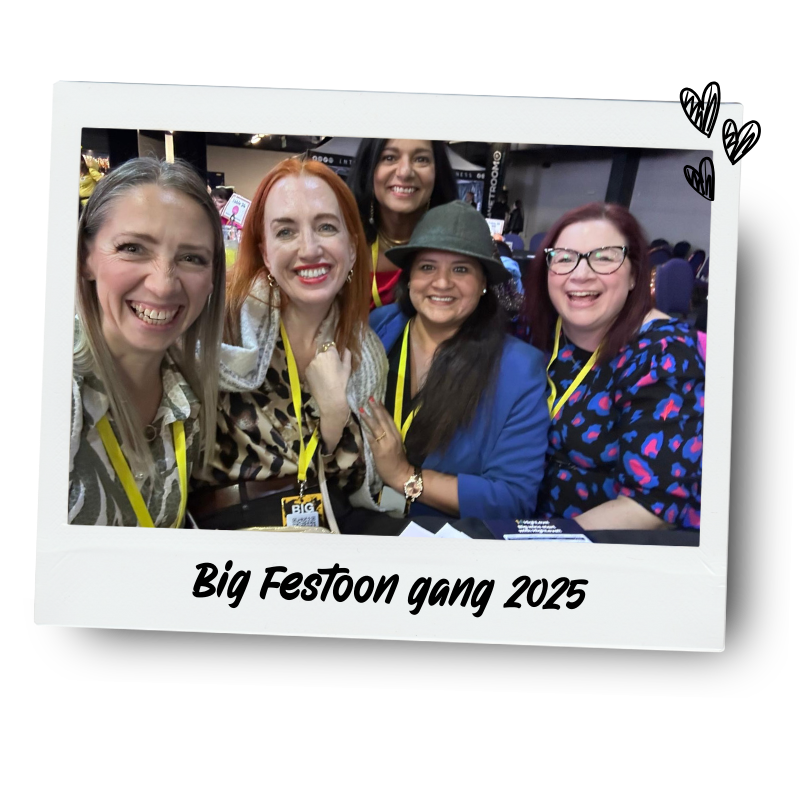 Five women smiling and posing for a photo at Big Festoon Gang 2025 event, with some wearing colorful clothing, a hat, and badges, inside a conference or event hall.
