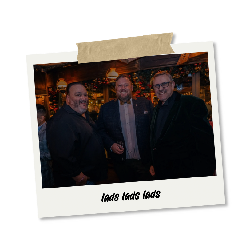 Three men smiling at a party, with Christmas decorations in the background, holding drinks, with the caption "Lads Lads Lads".