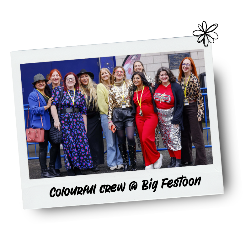 Group of women standing together outdoors, dressed in colorful outfits, smiling for a photo at Big Festoon.