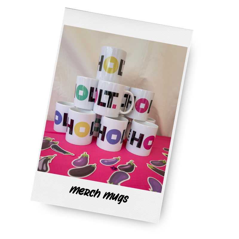 A collection of white ceramic mugs with colorful printed text, stacked in a pyramid shape on a pink surface, with eggplant stickers in front and the text 'merch mugs' at the bottom.