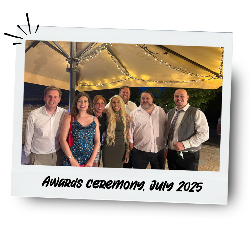 Group of seven people dressed in formal attire standing under a decorated canopy with string lights, at an awards ceremony in July 2025.