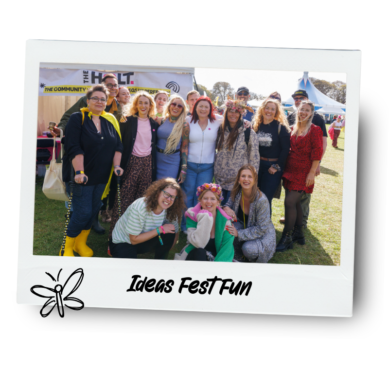 Group of people at Ideas Fest Fun event, outdoors with tents and banners in background, some wearing colorful or festive outfits, smiling for the camera.