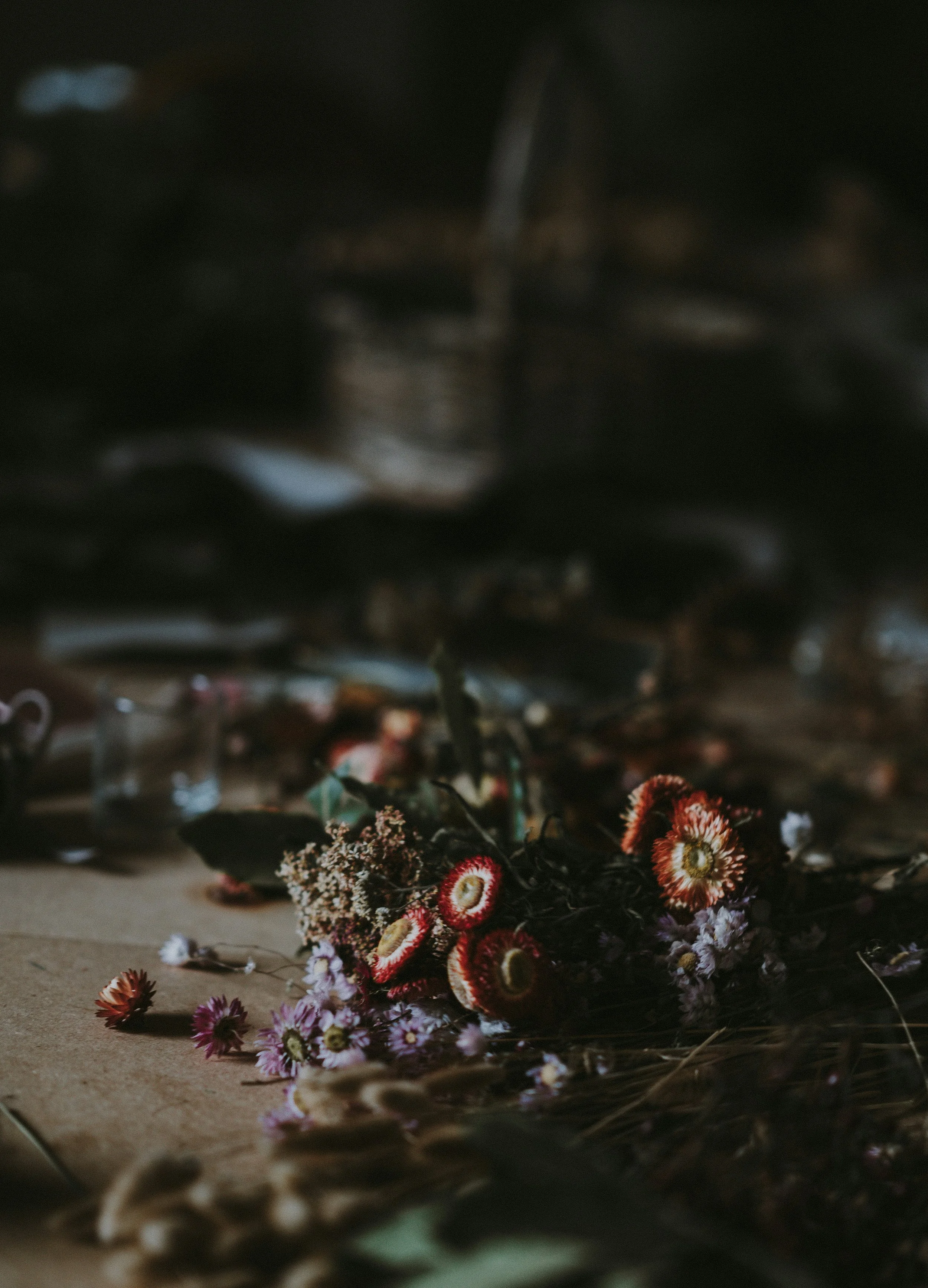 A pile of wilted and dried flowers scattered on a wooden surface with a dark, blurry background.