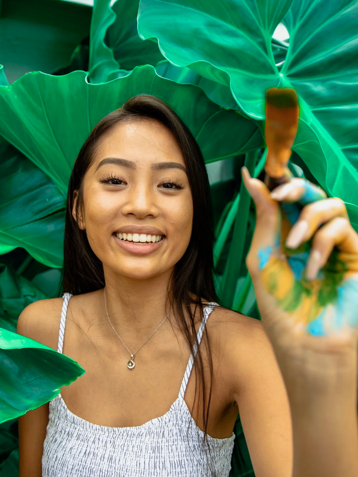 Creative outdoor portrait of a woman holding a paintbrush in tropical foliage