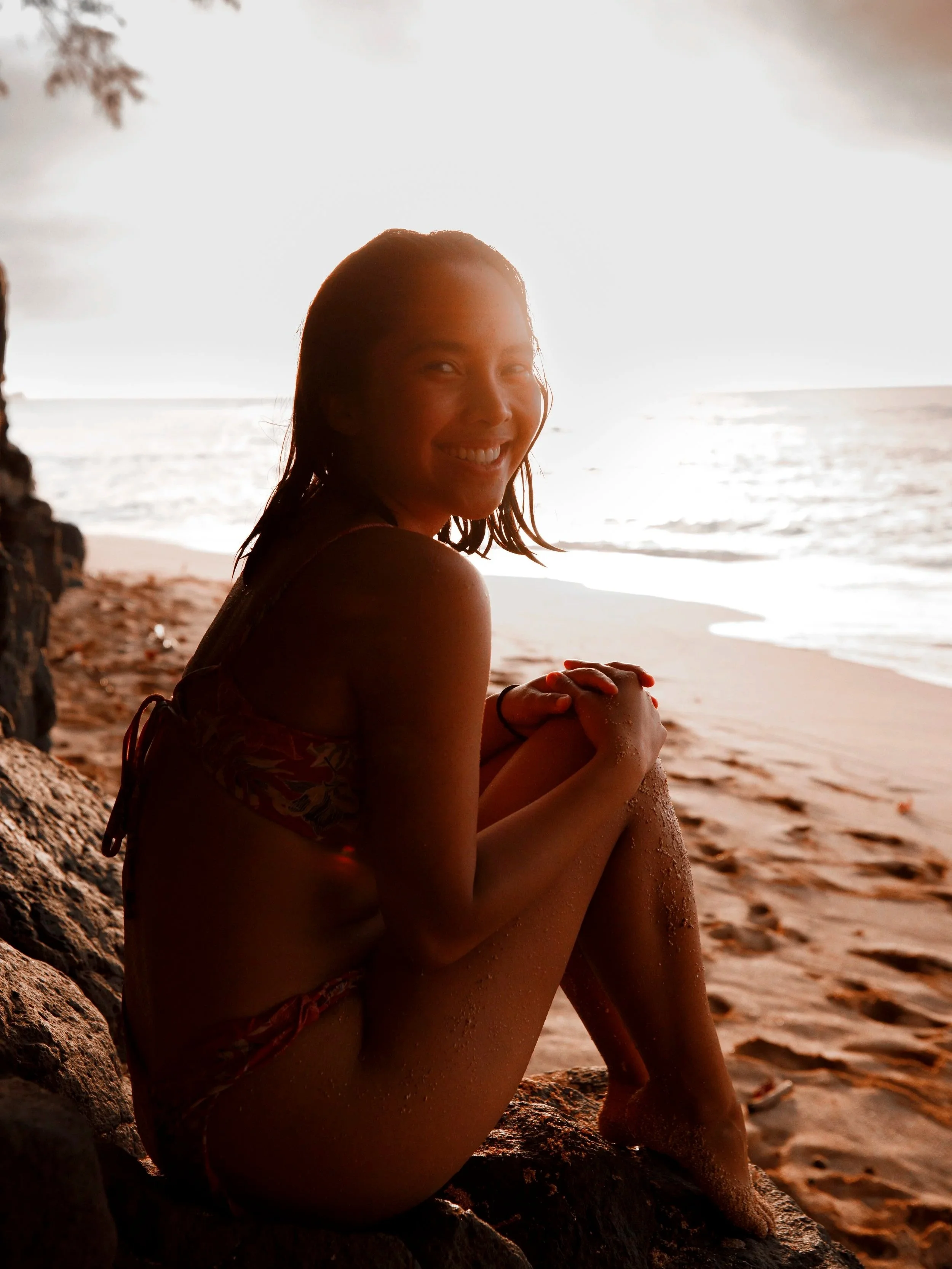 Outdoor beach portrait of a woman sitting on rocks at sunset