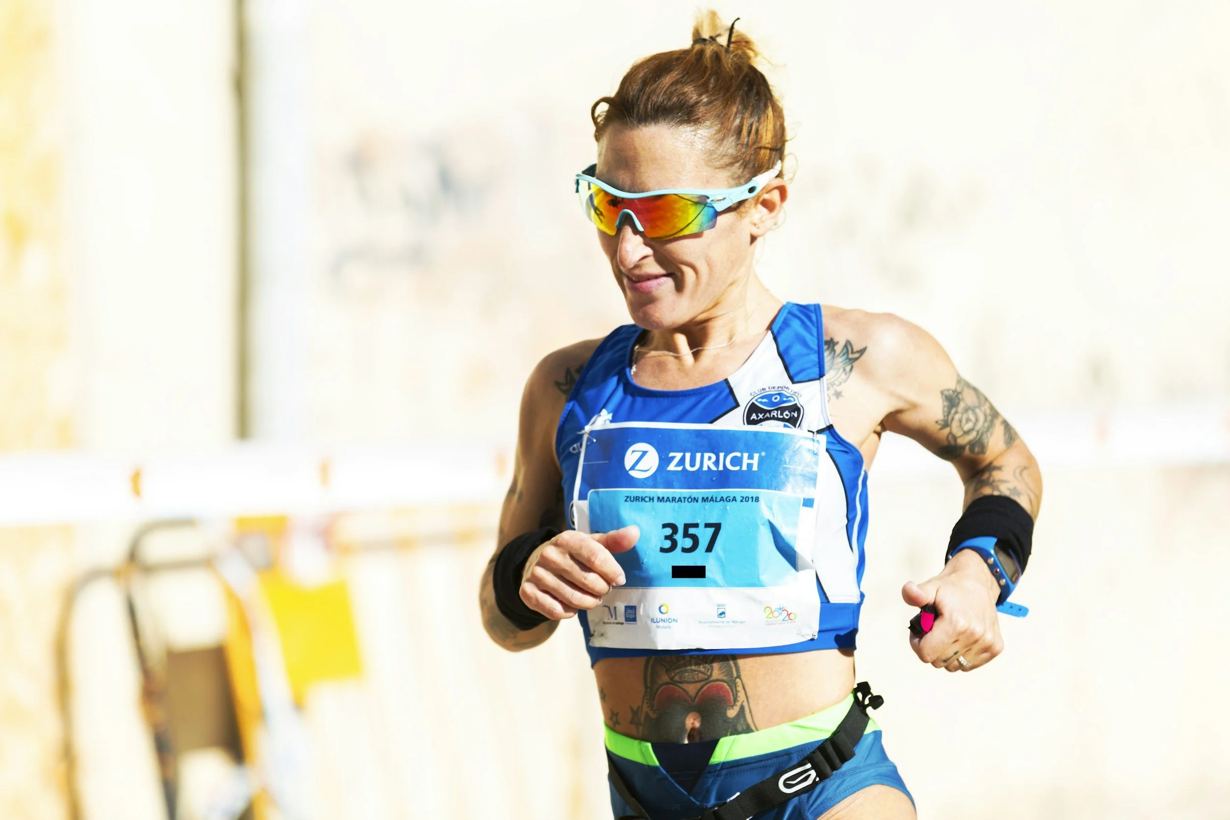 Female marathon runner wearing sunglasses, blue athletic attire, and a zebra-print waistband, running outdoors during daytime.