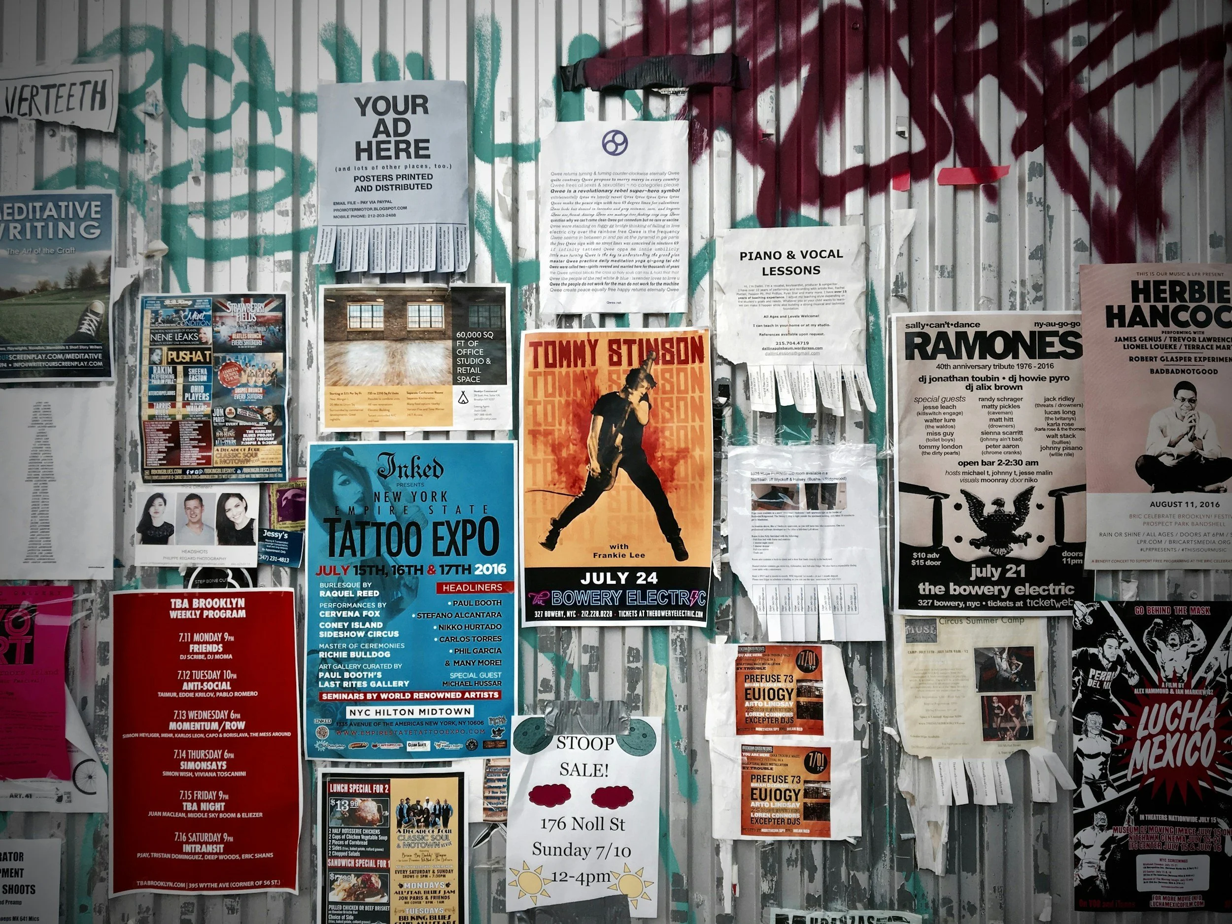 Bulletin board covered with various posters, flyers, and notices for events, performances, and services in an urban setting.