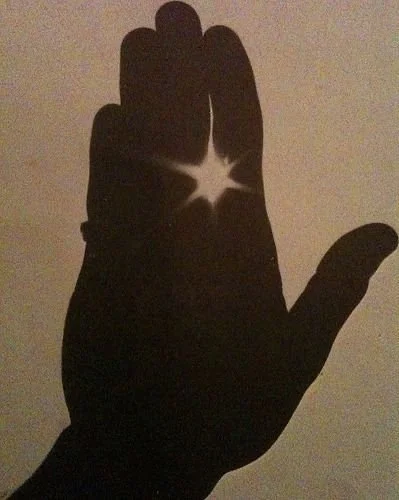 Silhouette of a hand with light shining through the fingers, creating a star-shaped glow.