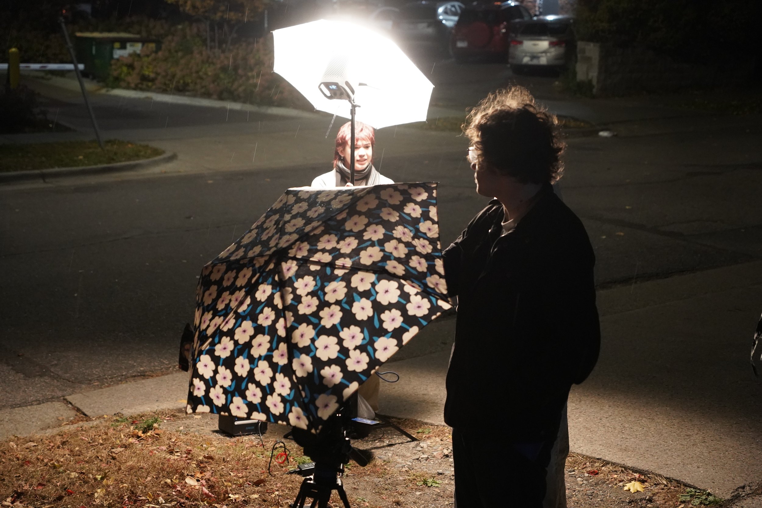 Eli Hayden, left, and Grant Hayden cover the camera and lights with umbrellas to shield them from the rain outside Bordertown Coffee in Minneapolis, Minn., on Nov. 2, 2025. Eli invited her brother, Grant, to help shoot the student short film “Girls’ 