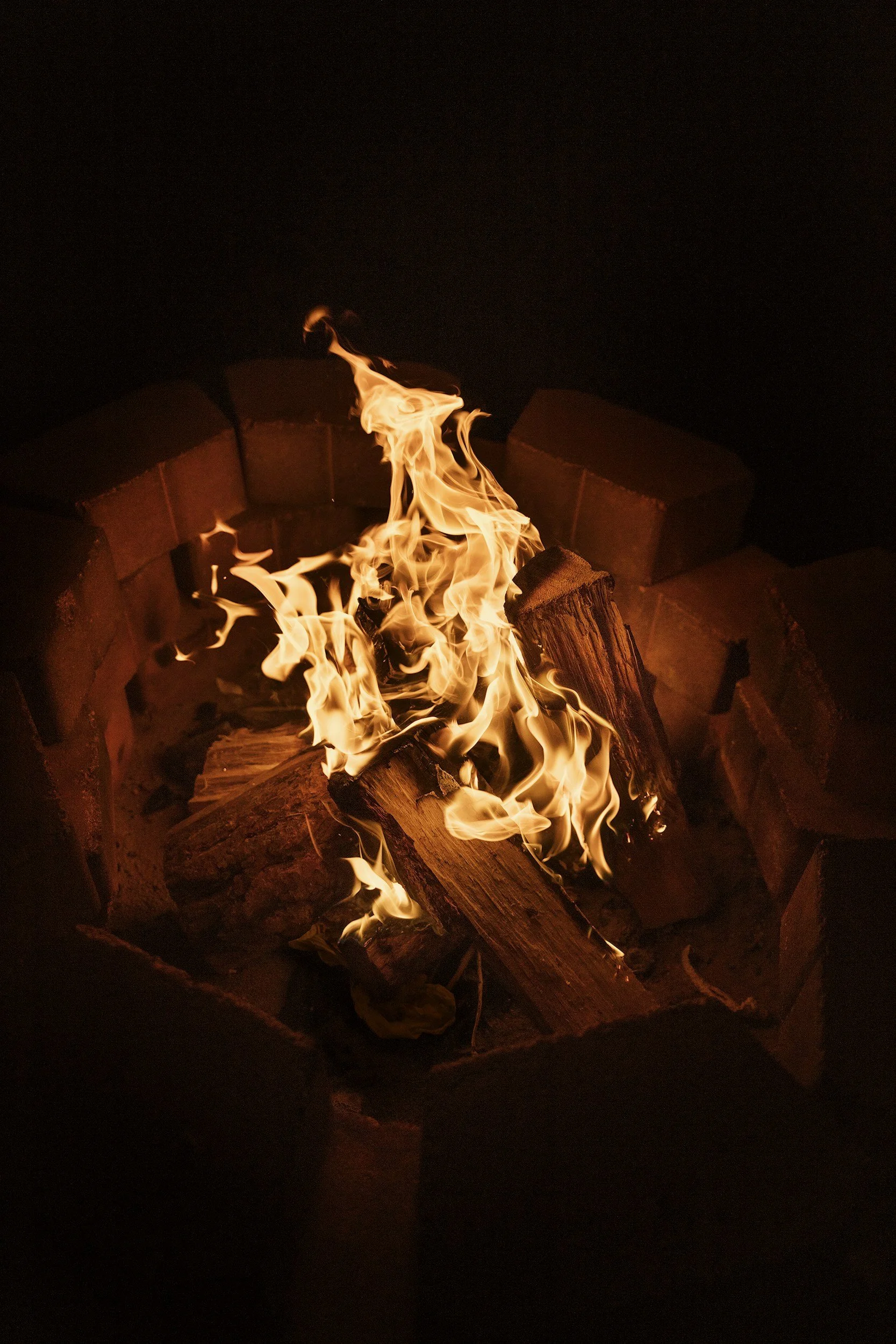 A campfire burning with orange flames and logs inside a fire pit at night.