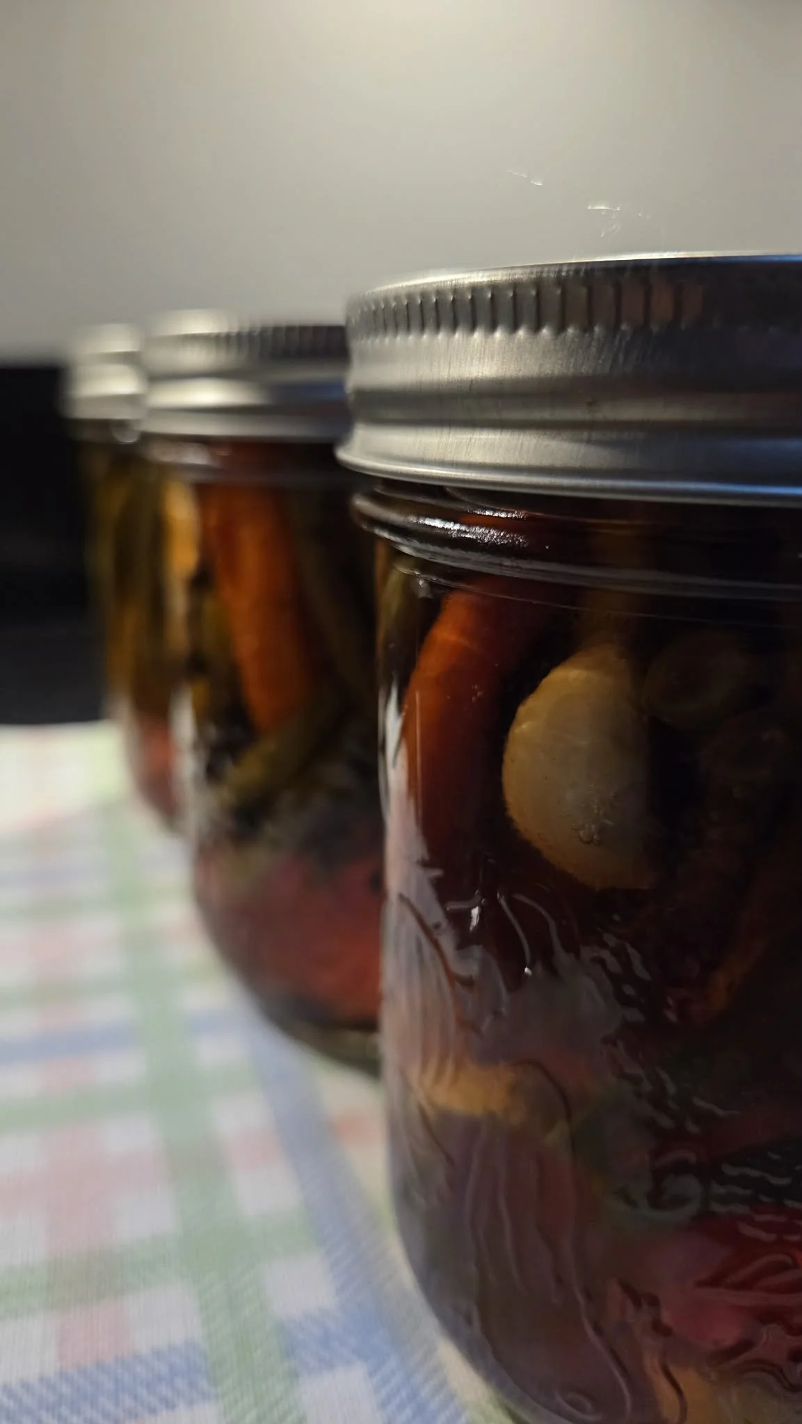 Close-up of glass jars filled with preserved marinated vegetables with metal lids.
