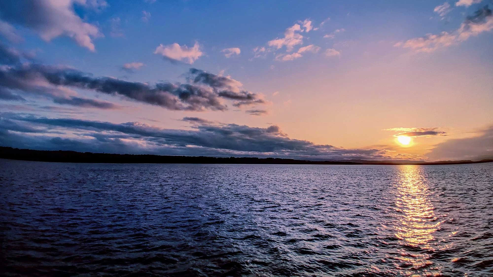 Sunset over a body of water with clouds in the sky.