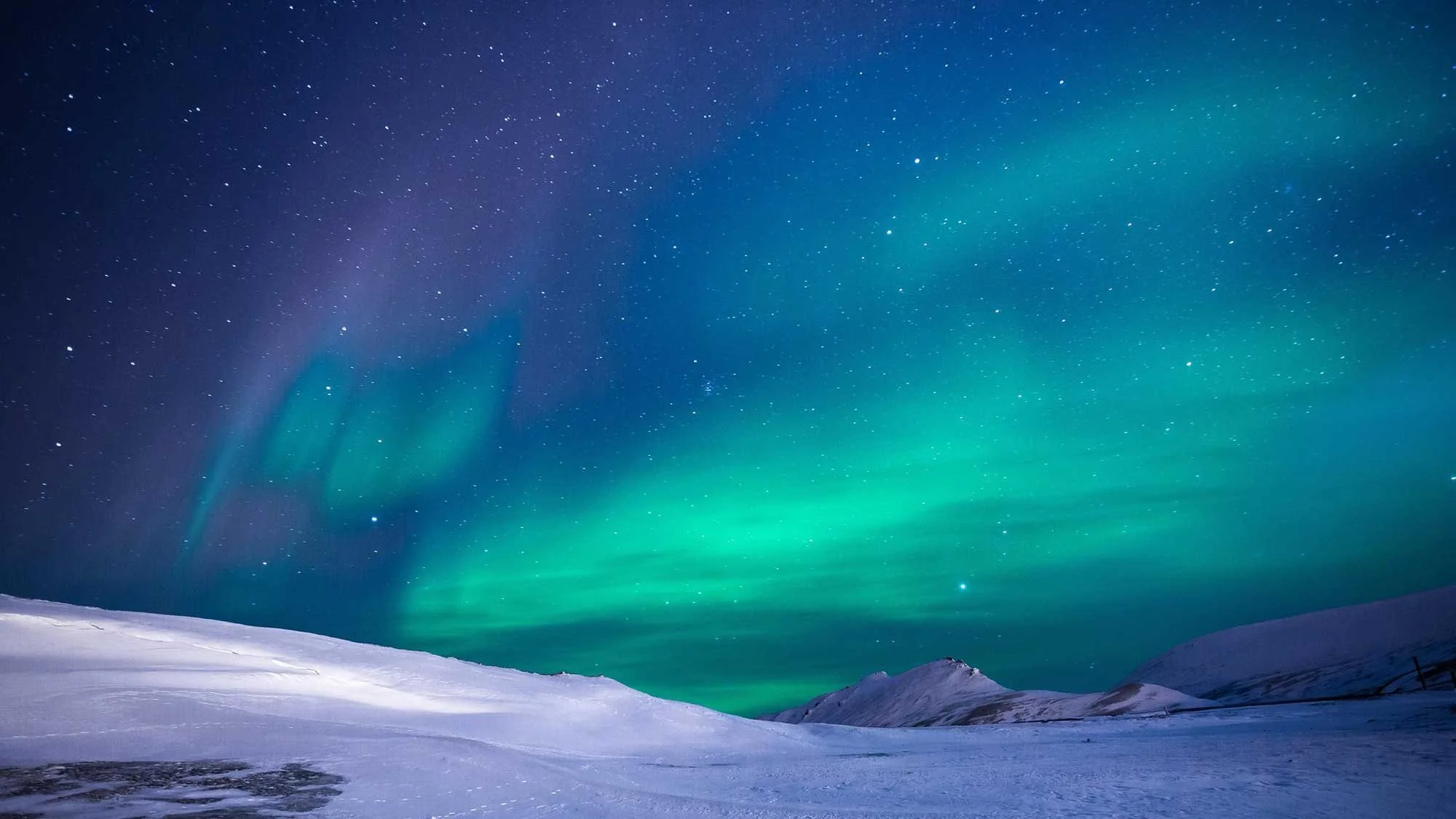 Night sky illuminated with the aurora borealis over snow-covered mountains and plains.