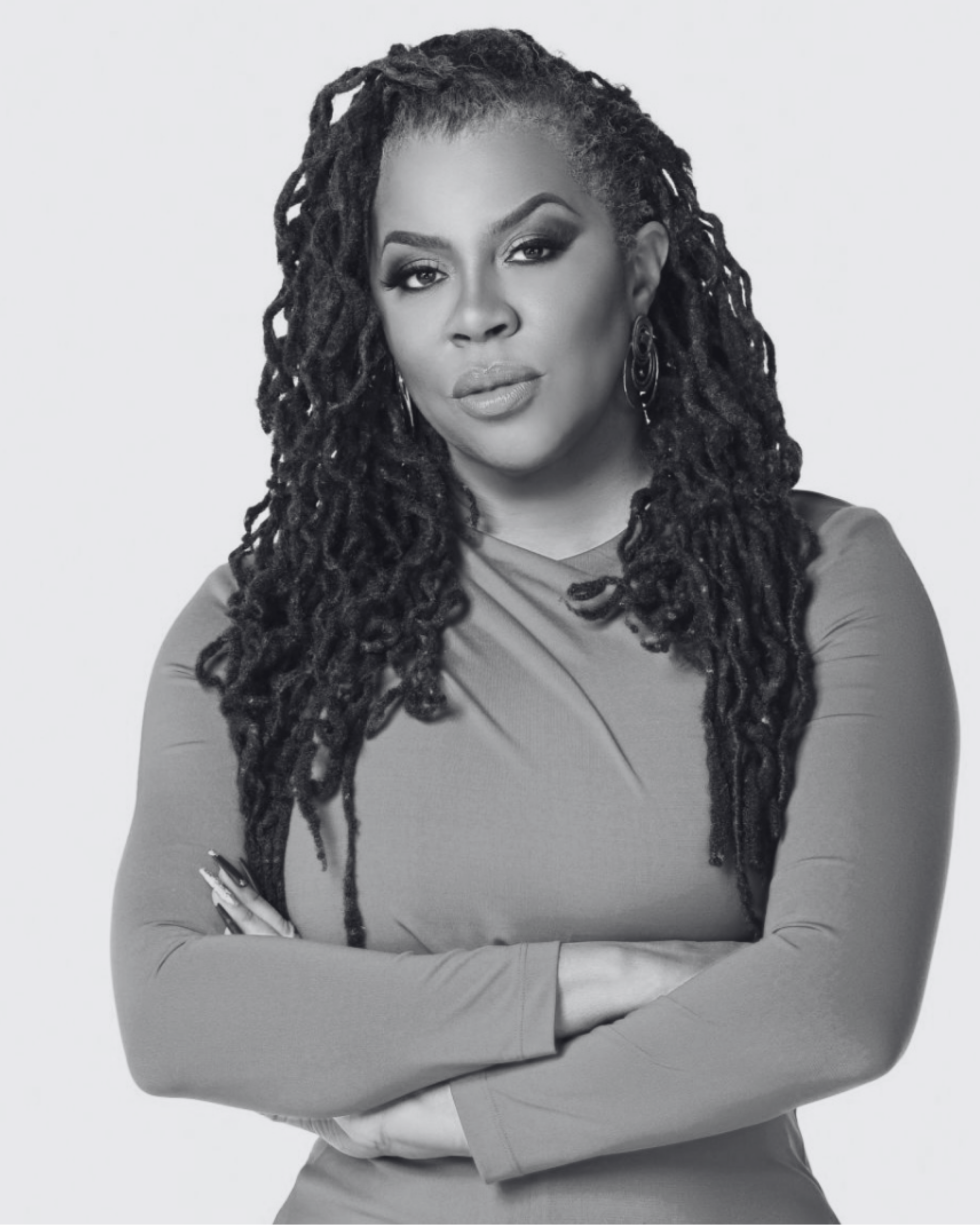 Black and white portrait of confident woman with long dreadlocks, crossed arms, earrings, and a fitted long-sleeve top, looking directly at the camera.