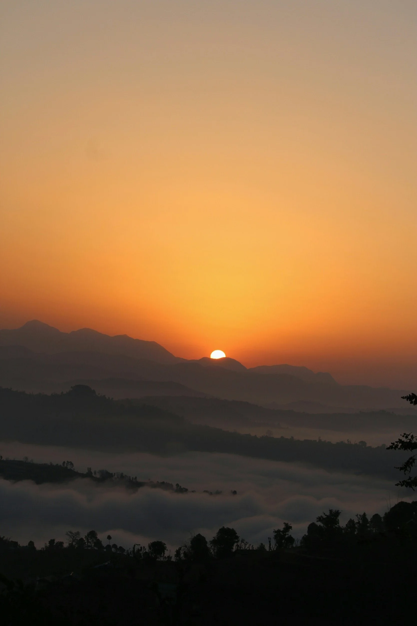 Sunset over a mountainous landscape with layers of hills and fog in the valleys.