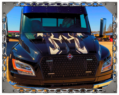 A black tow truck parked on a bridge at sunset, with a steel bridge structure and water visible in the background.