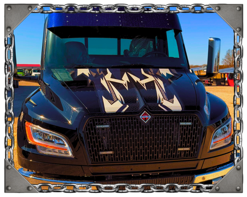 A black tow truck parked on a bridge at sunset, with a steel bridge structure and water visible in the background.