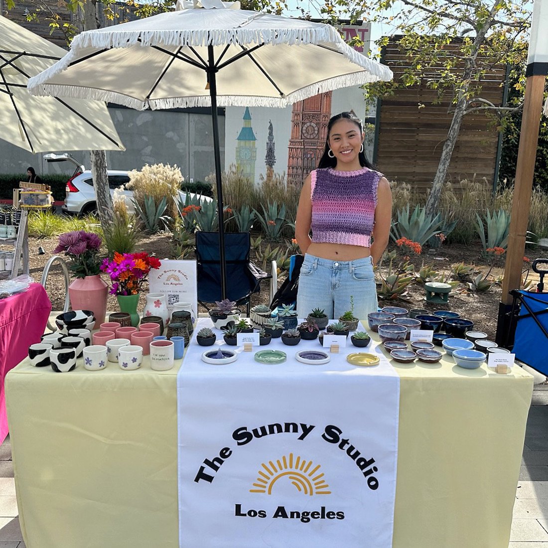 Christina standing behind her booth with colorful potteryat an outdoor craft market in Los Angeles.