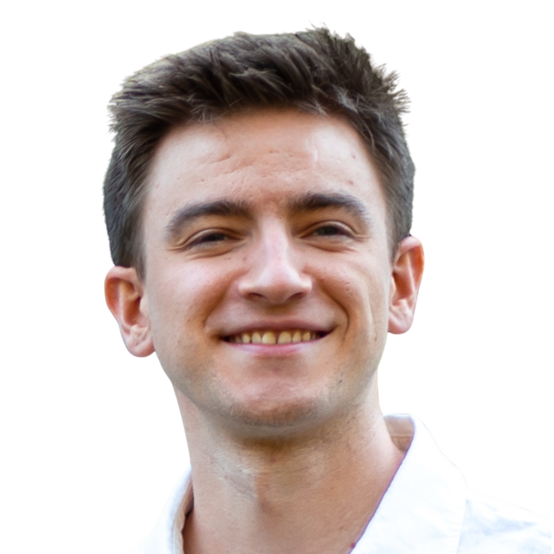 Close-up of a young man with short, dark hair, smiling, wearing a light-colored collared shirt.