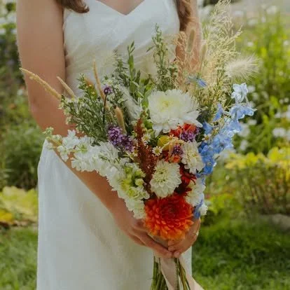 A woman in a white dress holding a colorful bouquet of flowers outdoors.