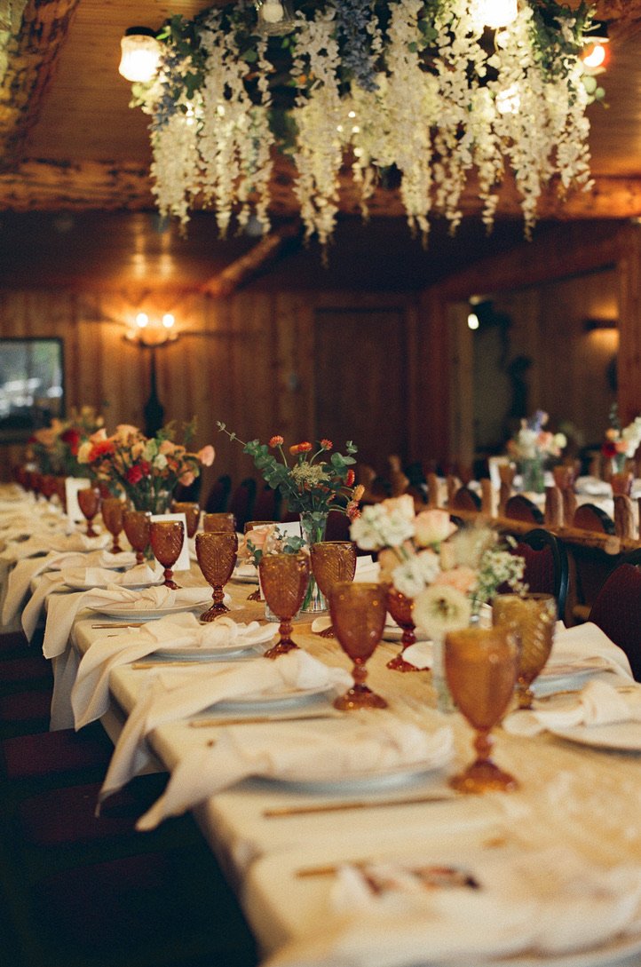 A full reception installation by Cherokee Bloom — farm-grown centerpieces and hanging floral chandelier in a wood-paneled Colorado venue.