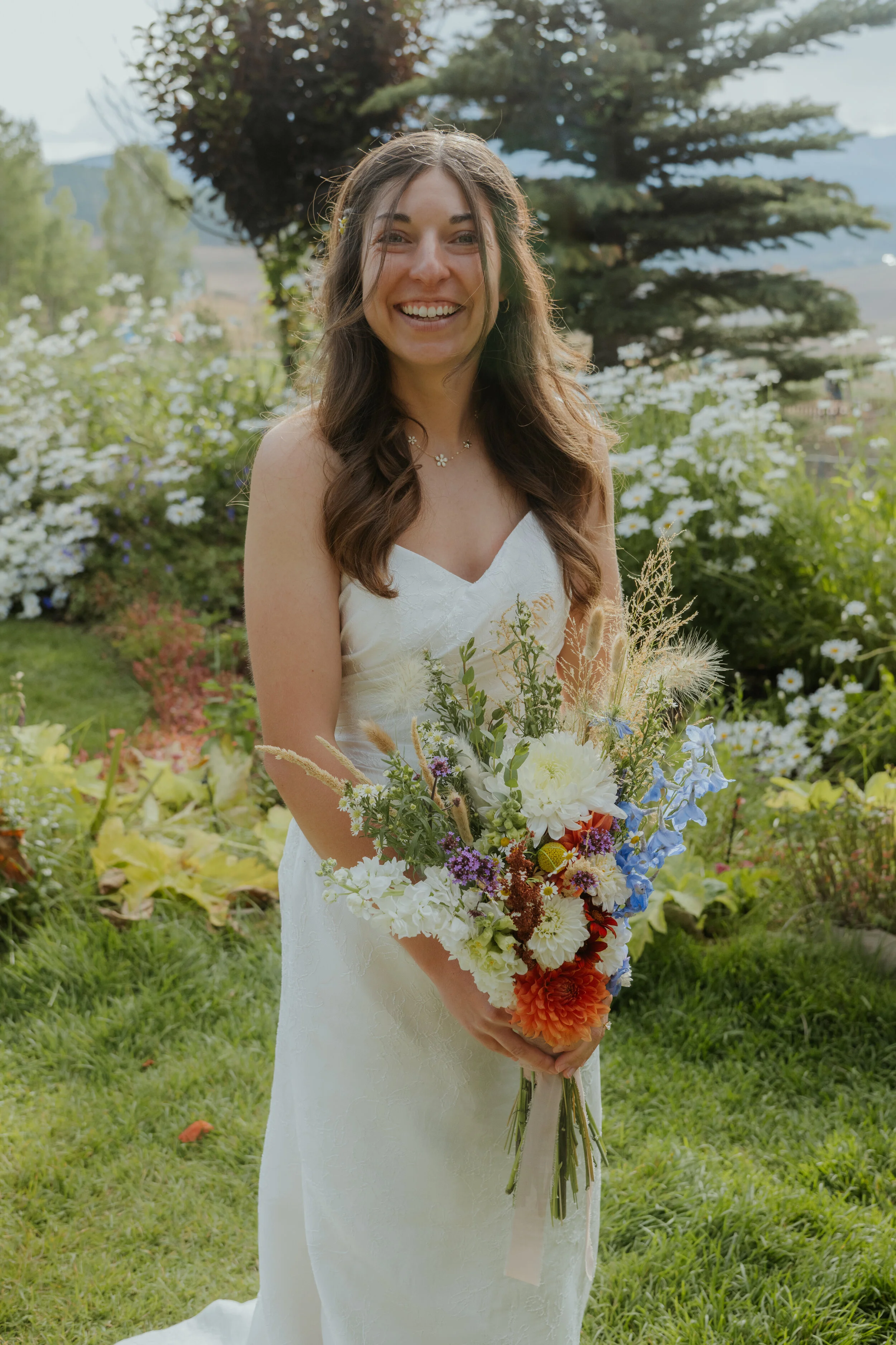 A bride holding a hand-tied bouquet of dahlias, snapdragons, and wildflowers grown at Cherokee Bloom's regenerative flower farm in Salida, Colorado.