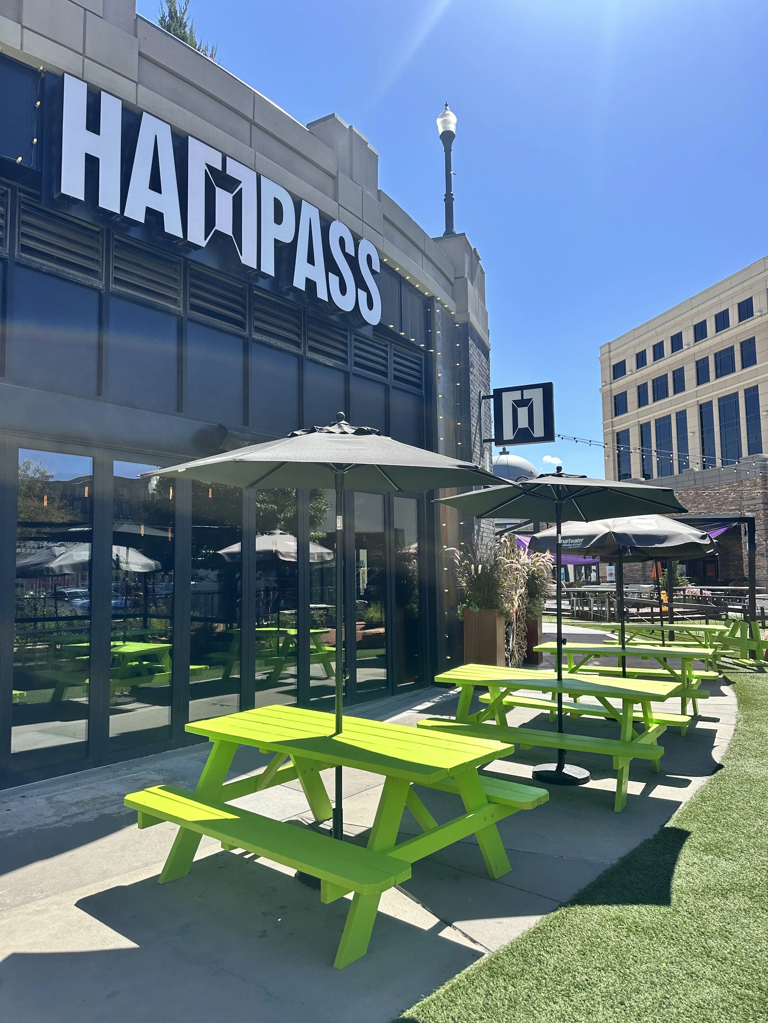 Outdoor seating area with bright green picnic tables and umbrellas at HapPass restaurant on a sunny day.