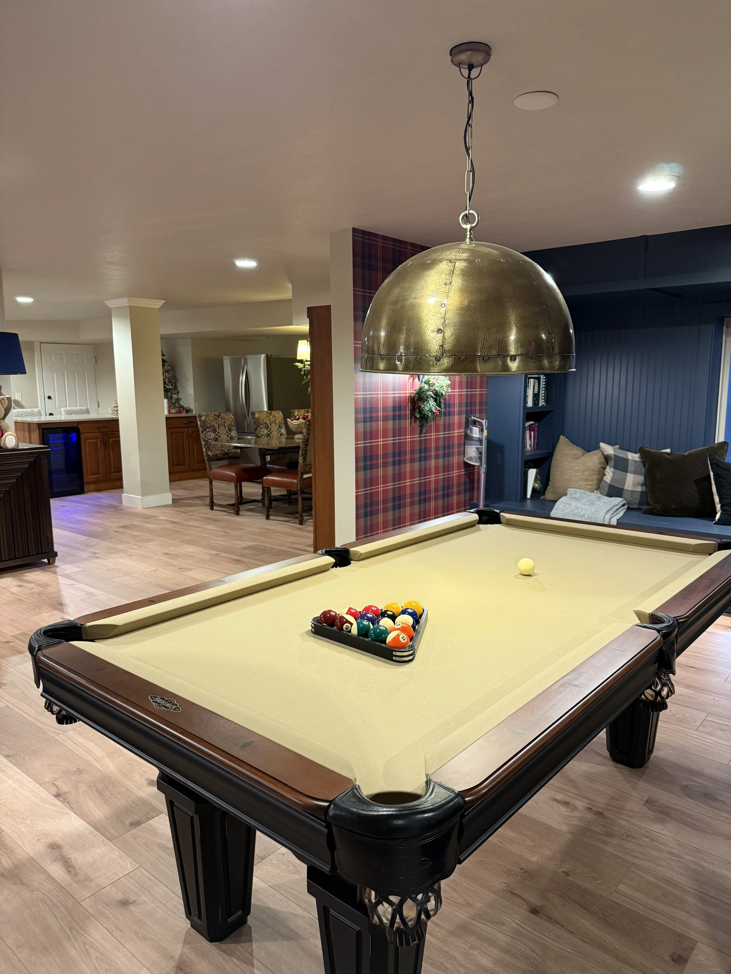 Pool table with billiard balls arranged on the felt surface and a cue ball nearby, hanging overhead light, in a cozy living room.