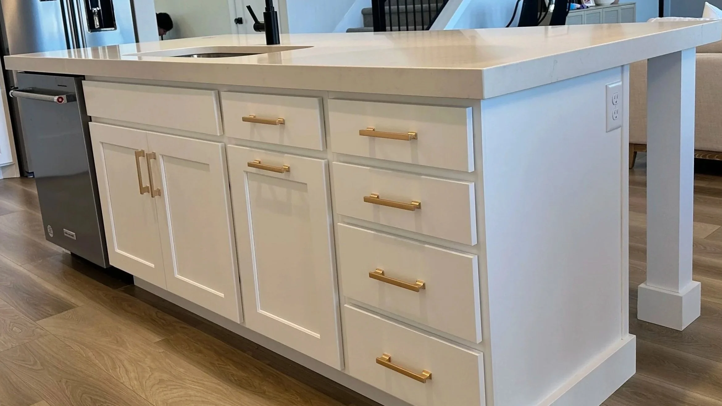 White kitchen island with gold handles, wooden flooring, and built-in sink and faucet.
