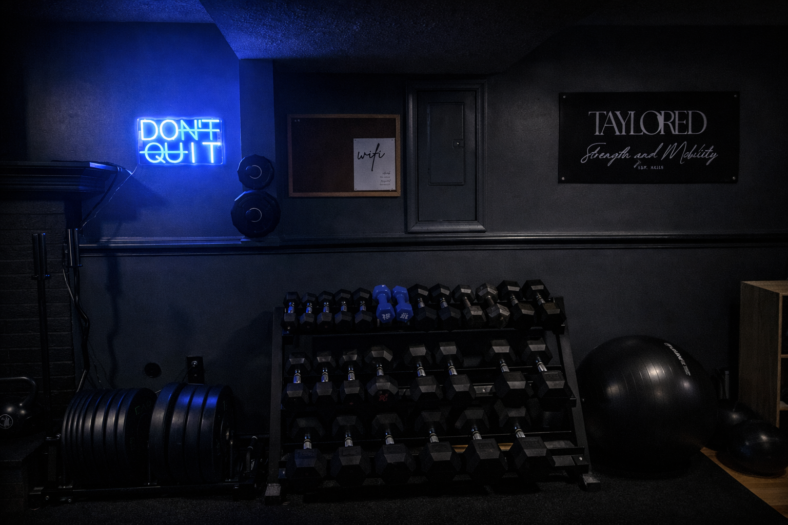 Dark gym room with a neon sign reading 'DON'T QUIT', dumbbell rack, exercise ball, and weights, illuminated dimly.
