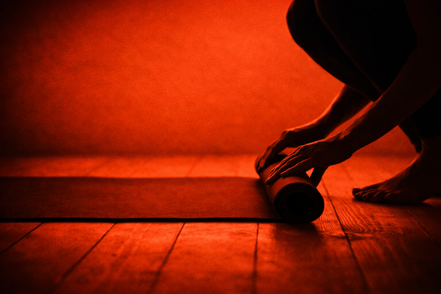 Person unrolling a yoga mat in a dimly lit room with warm, reddish lighting.