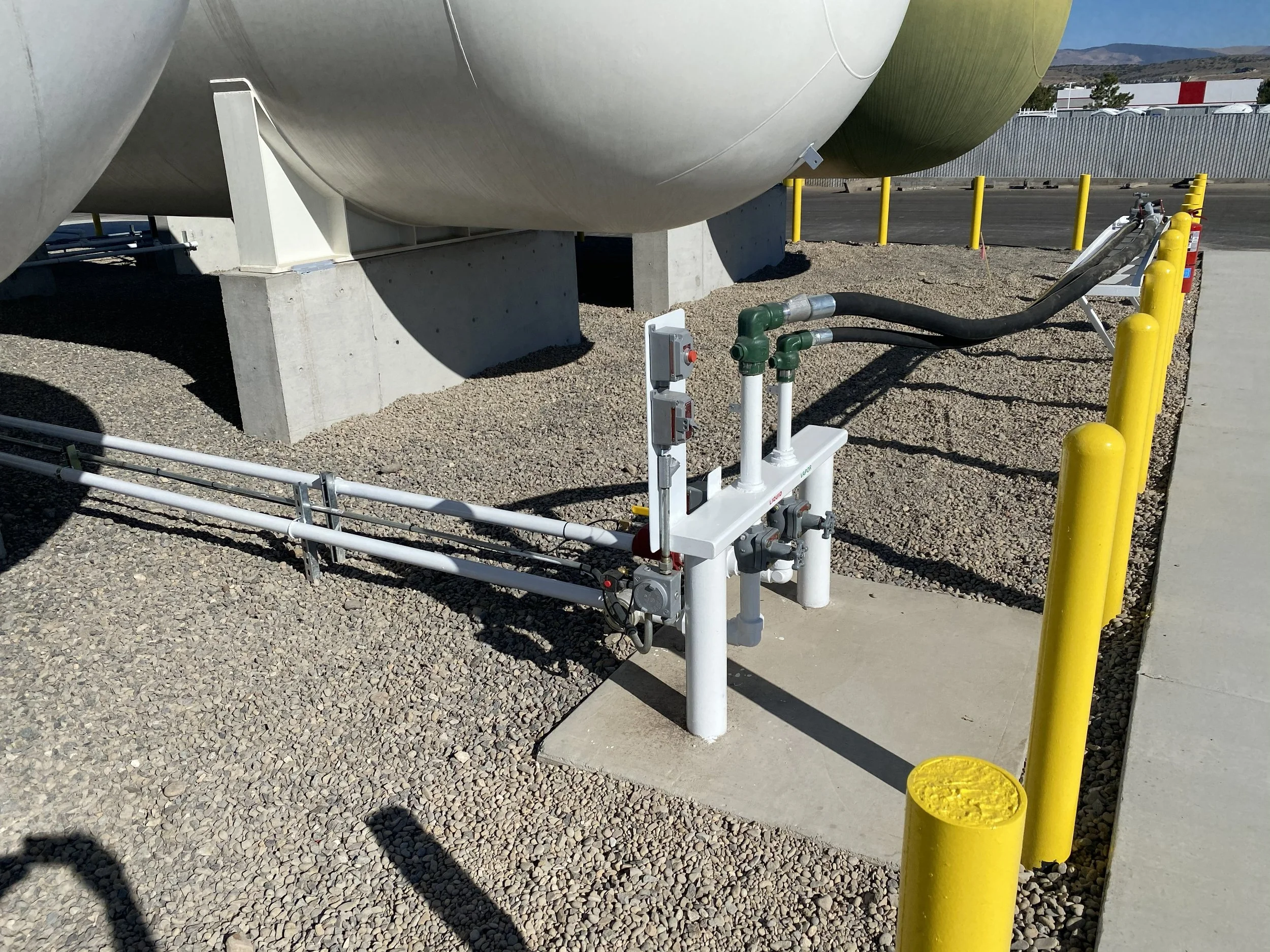 Close-up of bulk liquid propane storage tanks elevated on concrete bases, with attached distribution piping and safety barriers at a propane retailers storage facility.