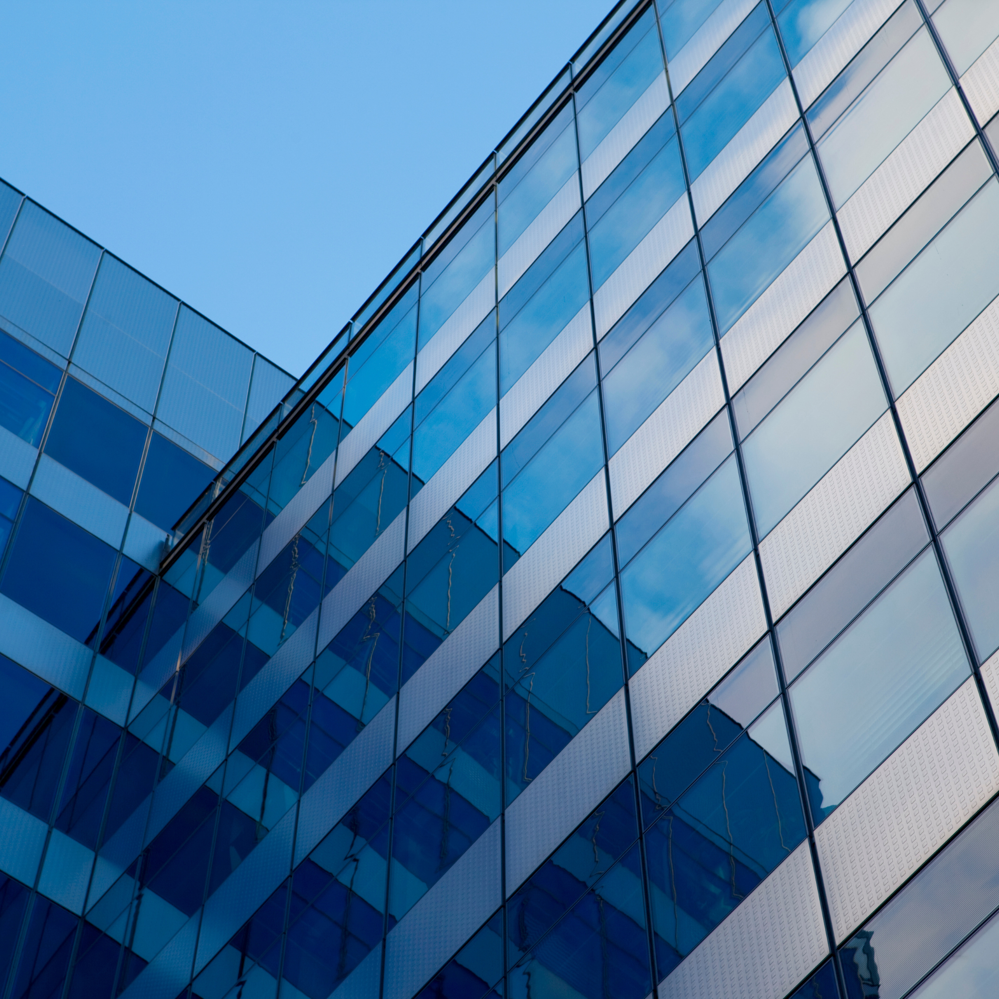 Close-up of a modern glass skyscraper reflecting the blue sky and white clouds.