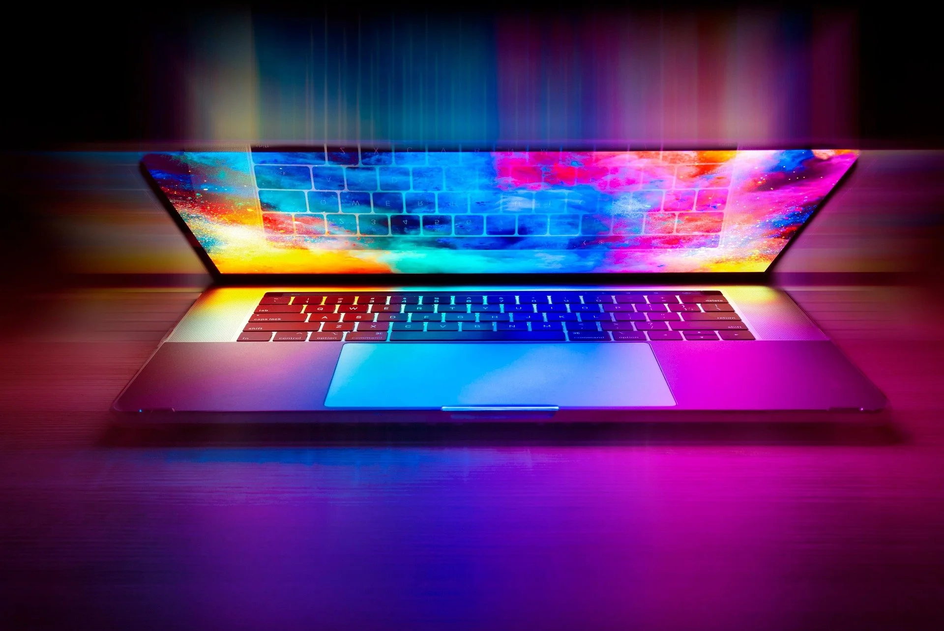 A laptop emitting colorful, vibrant light displays on the screen and keyboard in a dark setting.