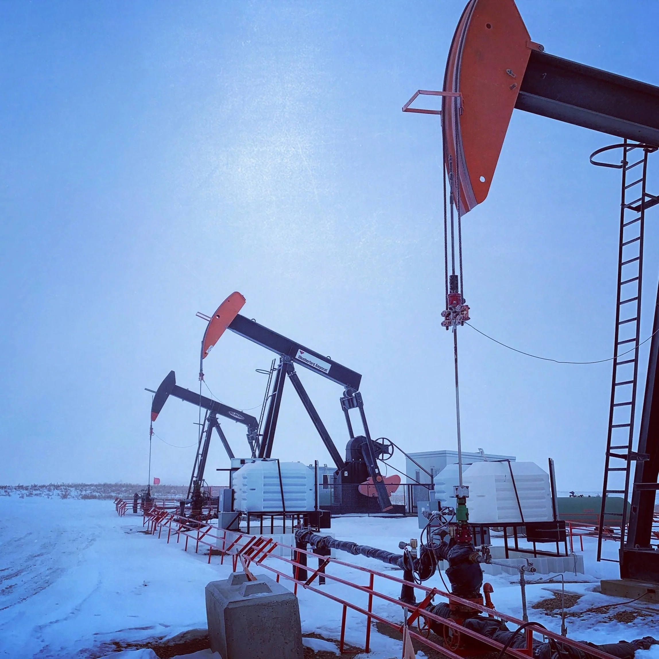Cold weather scene with oil pumpjacks company in a snow-covered landscape under a clear blue sky.