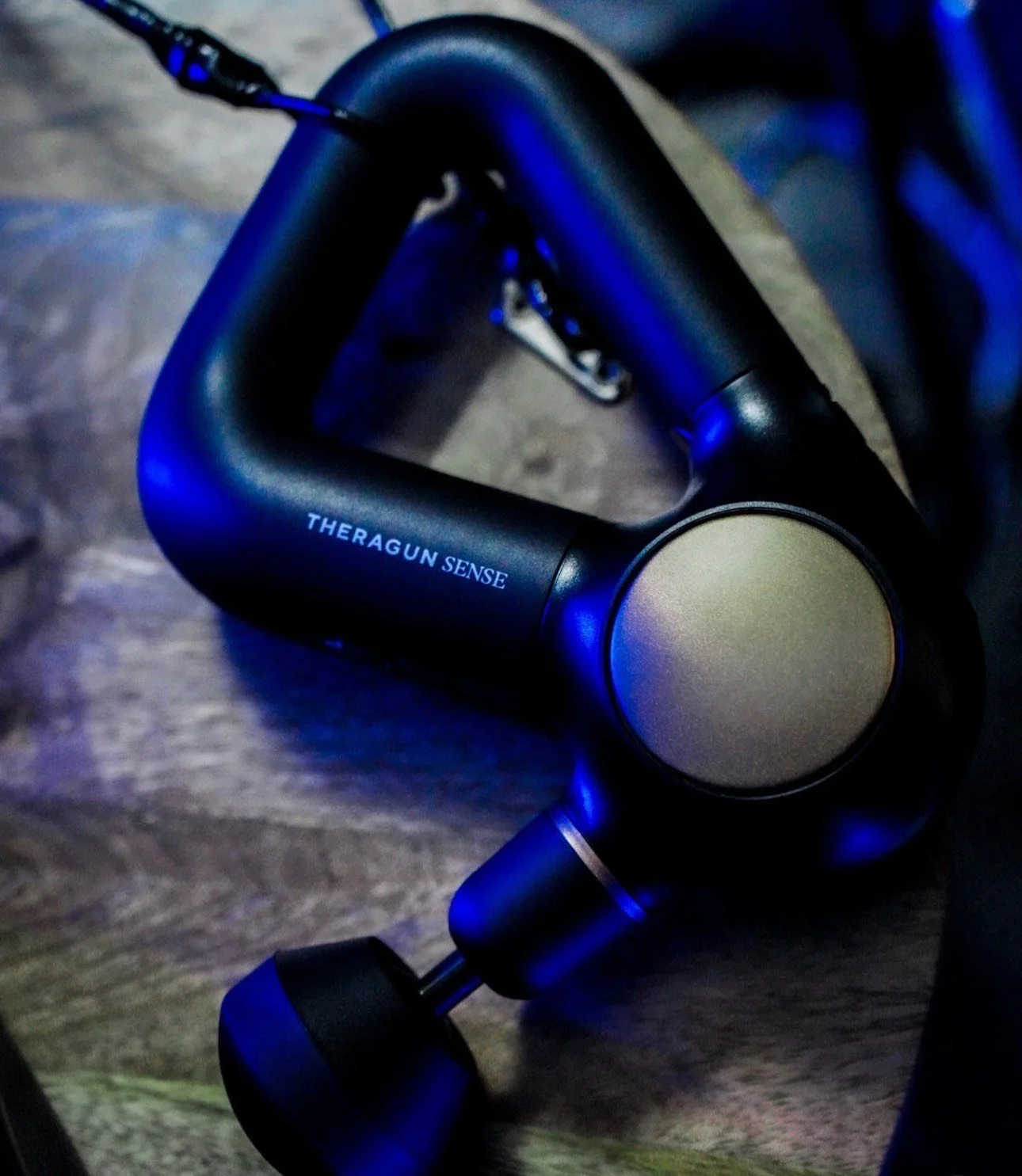 A black Theragun massage device laying on a wooden surface.