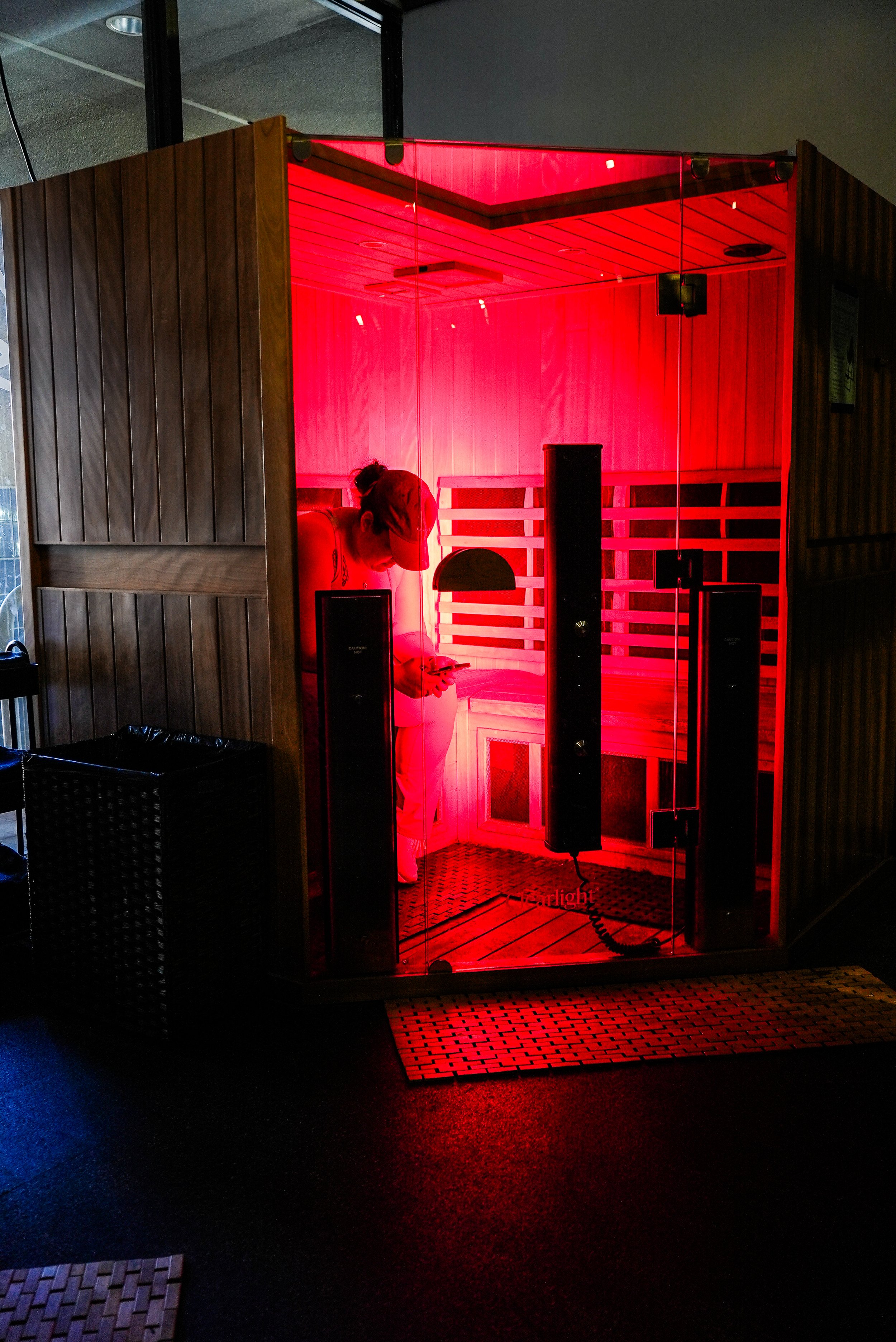A person standing inside a red-tinted infrared sauna, looking at their phone.