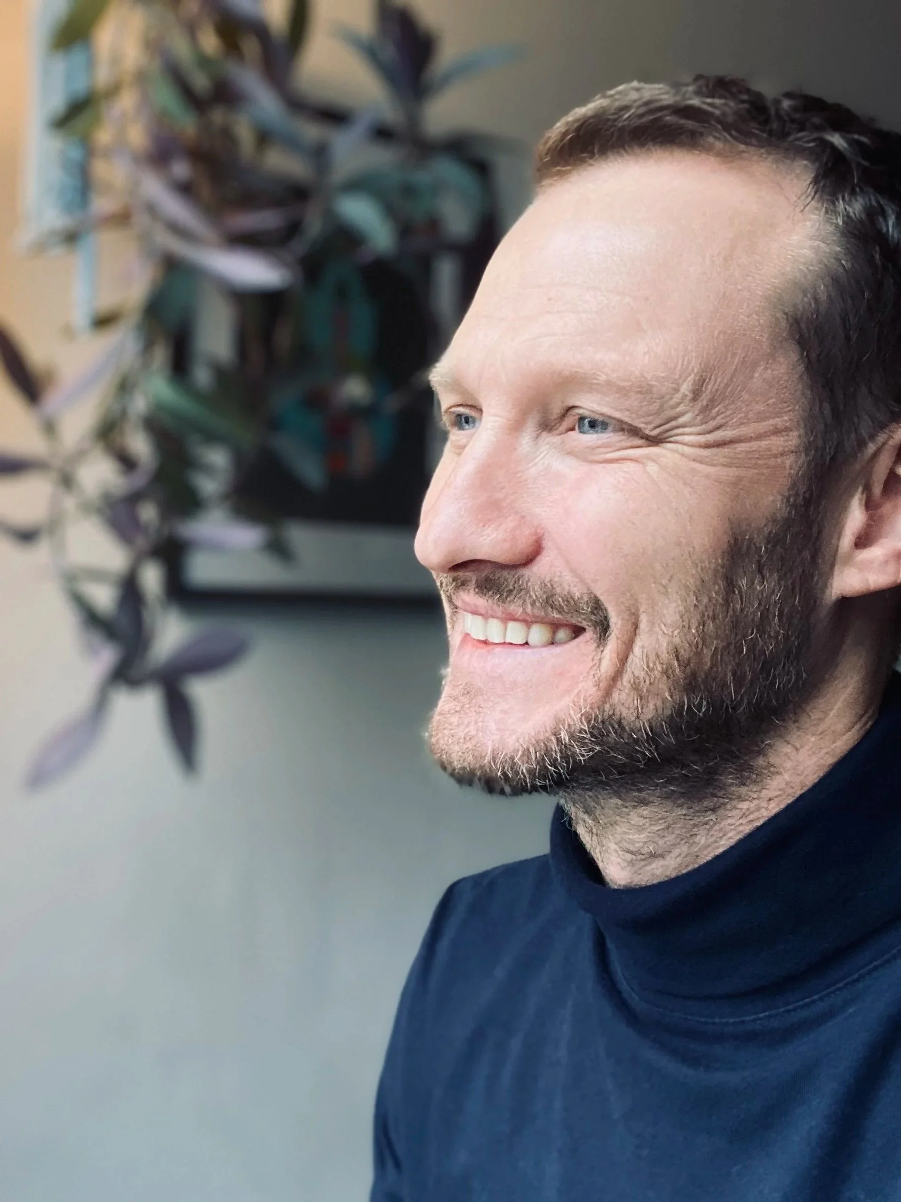 Man smiling looking to the left with a plant in the background